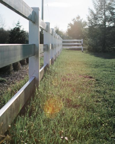 A vertical shot of gray wooden fences in a grass field during daytime